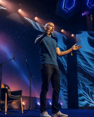 A speaker engaging the audience at the HOLOLIFE Summit 2026 in Amsterdam, set against a vibrant stage backdrop.