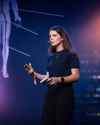 A speaker passionately presenting at HOLOLIFE Summit 2026, with a captivating background showing human anatomy.