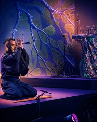 A performer in traditional attire engages in a meditative pose on stage during the HOLOLIFE Summit.