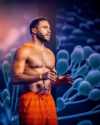 A speaker presents on stage at the HOLOLIFE Summit, showcasing themes of wellness and biohacking.