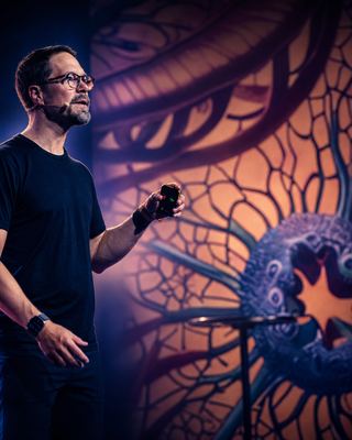 A speaker on stage passionately presenting at the HOLOLIFE Summit, with a vibrant backdrop illustrating the theme of longevity.