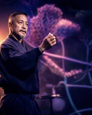 A speaker engaging the audience with a powerful gesture, set against a vibrant backdrop typical of the HOLOLIFE Summit.