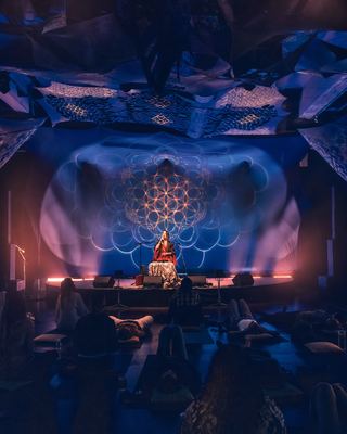 An intimate wellness session featuring a performer in a vibrant atmosphere with attendees lying on mats, engaged in relaxation.