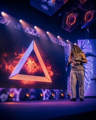 A speaker engages the audience on stage at HOLOLIFE Summit 2026, with a vibrant display in the background.