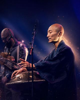 A performer plays a hang drum on stage, contributing to the ambient atmosphere of the HOLOLIFE Summit.