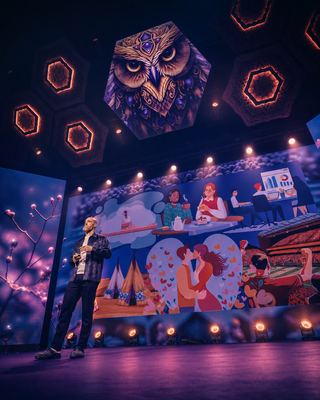 A speaker presents on stage, with vibrant visuals behind him, capturing the energy of the HOLOLIFE Summit 2026.