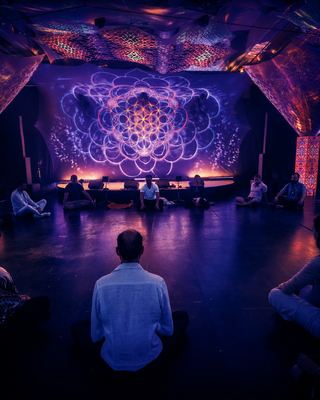 Attendees engage in a meditative session under a vibrant backdrop of illuminated art at HOLOLIFE Summit 2026.