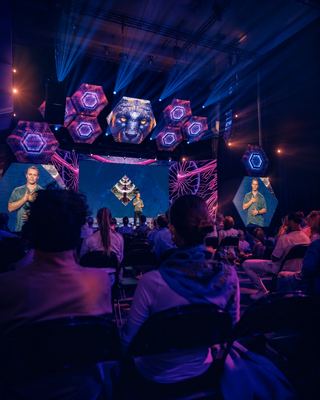 A speaker presents on stage with dynamic visuals in the background at the HOLOLIFE Summit 2026 in Amsterdam.
