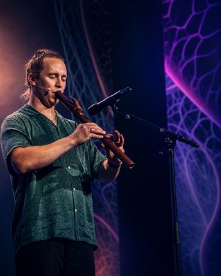 A performer plays a wooden flute on stage at the HOLOLIFE Summit 2026, enhancing the event's vibrant atmosphere.