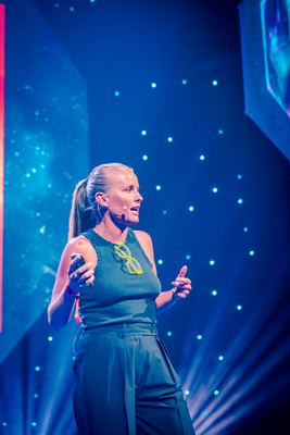 A speaker presenting insights on longevity at the HOLOLIFE Summit 2025 in Tallinn, surrounded by a vibrant, illuminated backdrop.