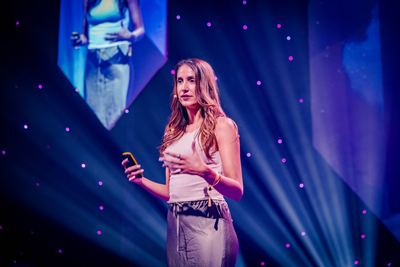 A speaker presents innovative ideas on stage at the HOLOLIFE Summit 2025, illuminated by dynamic lighting and projected visuals.