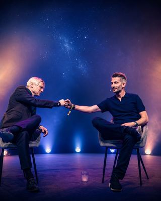 Two speakers engage in a fist bump on stage during a session at the HOLOLIFE Summit 2026.