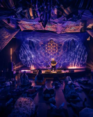 An immersive sound healing session at the HOLOLIFE Summit, featuring a musician surrounded by attendees lying on yoga mats, illuminated by vibrant lighting.