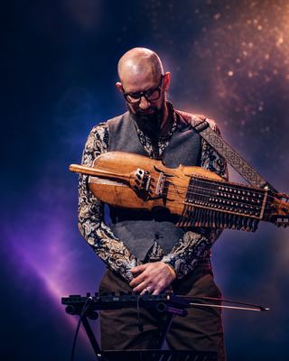 A musician prepares to perform on stage, showcasing a unique string instrument amidst vibrant lighting at the HOLOLIFE Summit.